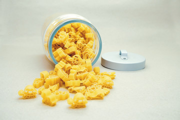 Baby eco-pasta from durum wheat in the form of animals falls out of a glass jar with lid on a light background. Yellow italian pasta in the form of animals on a beige background. Baby food.