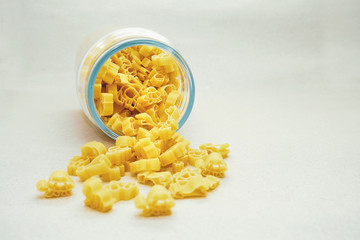 Children's eco-pasta from durum wheat in the form of animals falls out of a glass jar on a beige background. Yellow pasta in the form of animals on a beige background. Baby food.