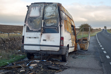 The burned out wreckage of an old van in a road layby 