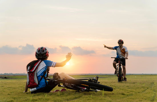 Woman riding mountain bike was accident crashed and fell to the grass while a lover her coming in to help at the beautiful sunset time. Using help and giving family love concept. © Love You Stock