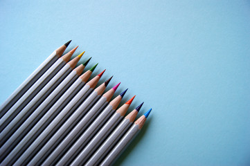 Many color pencils lies on light blue background. Art concept