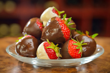Strawberries dipped in dark and white chocolate stacked on a glass saucer
