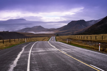 the long local road across yellow and green grass field goto mountain that have cloud on behind like a heaven