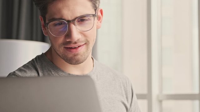 Young pleased positive man indoors at home using laptop computer