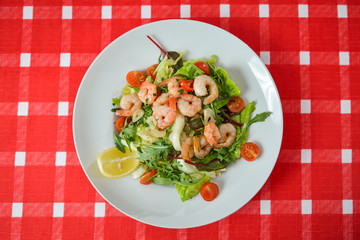 Vegetable salad with shrimp on white plate on red-white tablecloth