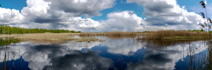 Obraz premium Panoramic view of a calm lake with white cumulus clouds