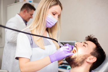 Obraz na płótnie Canvas Happy young female Caucasian dentist drilling out dental cavity and preparing the tooth for filling. Young man having his teeth checked in a dental clinic