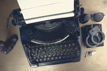 Desktop of a police investigator. Typewriter, handcuffs, whistle and dark glasses on the table. Soft focus.