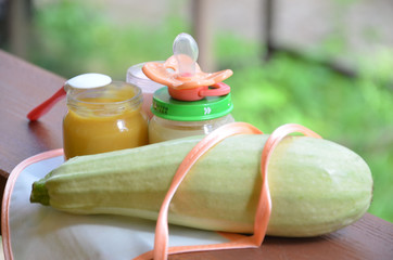 Baby food in jars puree mashed food on a background of foliage, With Zucchini a pacifier and spoon