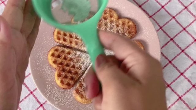 Powdered sugar sprinkled on to heart shaped waffles, Bakery concept. With noise and burry bokeh background.