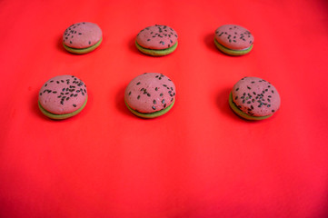 Multi-colored green and pink, bright cookies with two halves dressed with filling and sprinkled with sesame seeds on a bright pink color background.