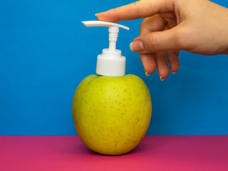 Fresh green apple with white dispenser for cosmetics, soap and other hygiene products on blue and pink background. Useful fruit.