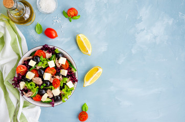 Salad with tuna, fresh vegetables, olives and feta cheese in a bowl on a light blue concrete background. Healthy food. Horizontal orientation. Top view, copy space.