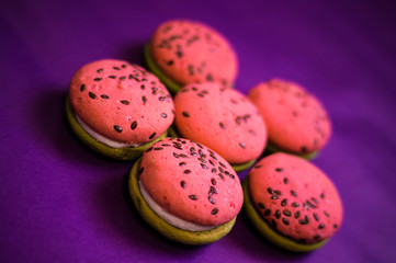 Obraz na płótnie Canvas Multi-colored green and pink, bright cookies with two halves dressed with filling and sprinkled with sesame seeds on a bright purple color background.