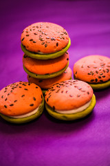 Multi-colored green and pink, bright cookies with two halves dressed with filling and sprinkled with sesame seeds on a bright purple color background.