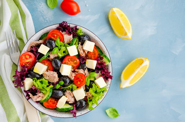 Salad with tuna, fresh vegetables, olives and feta cheese in a bowl on a light blue concrete background. Healthy food. Horizontal orientation. Top view, copy space.