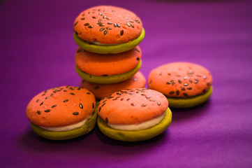 Multi-colored green and pink, bright cookies with two halves dressed with filling and sprinkled with sesame seeds on a bright purple color background.