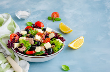 Salad with tuna, fresh vegetables, olives and feta cheese in a bowl on a light blue concrete background. Healthy food. Horizontal orientation. Copy space