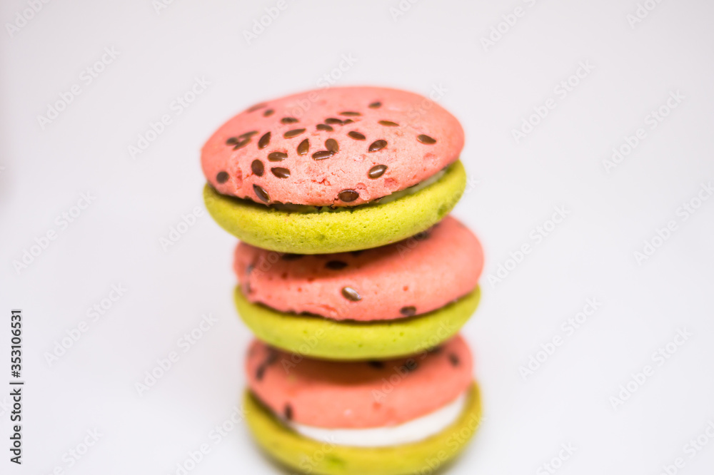 Wall mural Multi-colored green and pink, bright cookies with two halves dressed with filling and sprinkled with sesame seeds on a bright white color background.