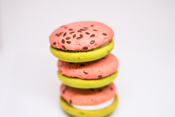 Multi-colored green and pink, bright cookies with two halves dressed with filling and sprinkled with sesame seeds on a bright white color background.