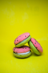 Multi-colored green and pink, bright cookies with two halves dressed with filling and sprinkled with sesame seeds on a bright yellow color background.