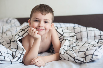 A boy with brown hair and brown eyes is smiling as he lies on the bed