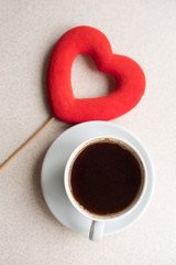 Cup of coffee with red felt heart on white background, close up. Place for text. Valentine's day celebration concept, top view. Vertical photo
