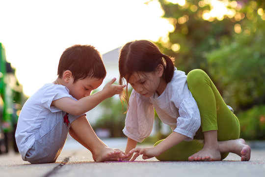 Sibling Asian kids playing or painting on ground.Kid sitting and drawing with bare foot.Concept of natural childhood.Simple and nice life style.Down to earth concept.