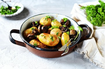 Baked young potatoes with mushrooms in a bowl on a gray background