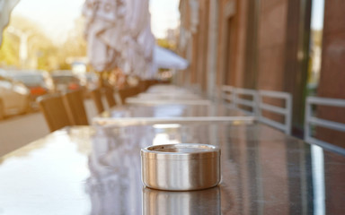 Empty summer terrace with ashtray on metal table at coffee house and restaurant beside sidewalk in...