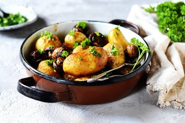 Baked young potatoes with mushrooms in a bowl on a gray background
