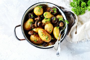 Baked young potatoes with mushrooms in a bowl on a gray background