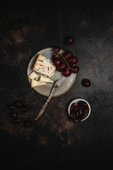Blue cheese and grape, olives and dates on grey plate with knife on brown concrete background, copy space, wine snack