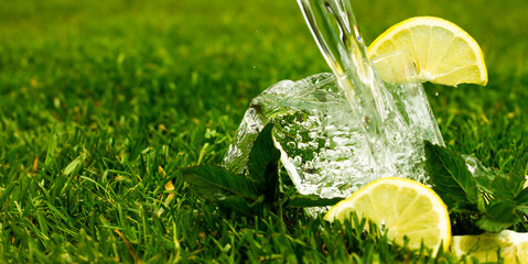 Glass of sparkling water or lemonade with lemon and mint leaves. Water with splashes and drops flows into a glass. Banner.