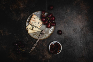 Blue cheese and grape, olives and dates on grey plate with knife on brown concrete background, copy space, wine snack