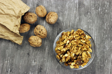 Walnut kernels in a bowl and whole nuts on an old gray table