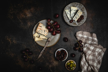 Blue cheese and grape, olives and dates on grey plate with knife on brown concrete background, copy space, wine snack