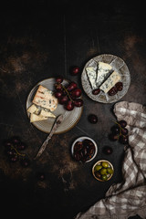 Blue cheese and grape, olives and dates on grey plate with knife on brown concrete background, copy space, wine snack