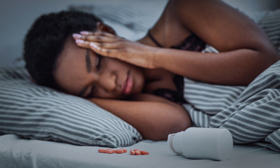 Obraz na płótnie Canvas Pills sprinkled from jar on bed, african american girl cannot fall asleep