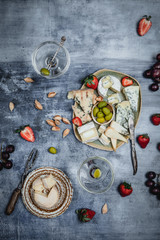 Fototapeta na wymiar variety of cheese with fresh strawberries, grape, olives and nuts, martini glasses on shabby blue background, top view, party appetizer concept