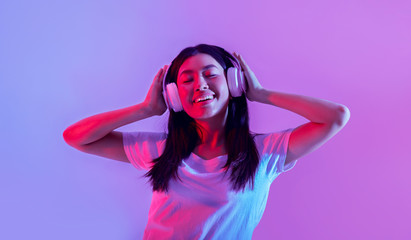 Happy asian girl in big headphones expresses emotions of pleasure from song