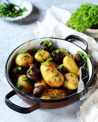 Baked young potatoes with mushrooms in a bowl on a gray background