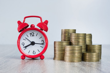 Red alarm clock And a pile of coins placed on the table Time concepts and investing during tax periods, time limits for saving money.