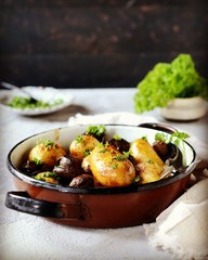 Baked young potatoes with mushrooms in a bowl on a gray background