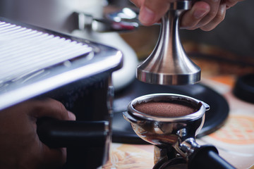 Close-up view of on hands barista presses ground coffee using tamper.