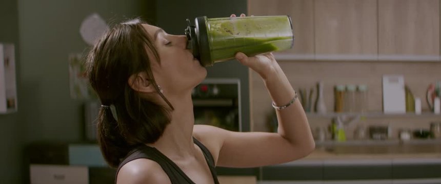 Portrait of fit female drinking green juice detox cocktail in the kitchen at home. Shot with 2x Anamorphic lens