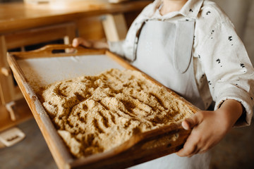 Boy wearing an apron, holding a wooden tray with freshly ground cornmeal.