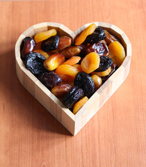 dried apricots, prunes and dates in a heart-shaped wooden bowl