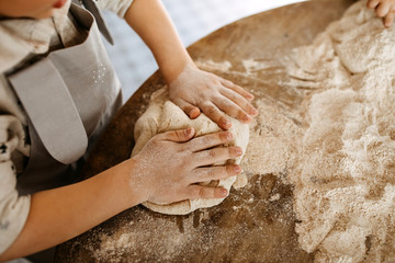 Child making dough for bread, mixing flour on a wooden table surface.