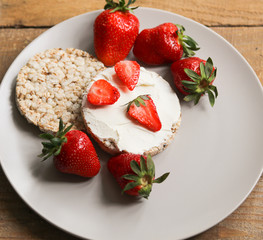 crispbreads with cottage cheese and strawberries on a white plate on a wooden table close up